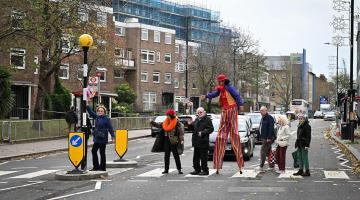 Maystar Residents’ Association committee members, including Debbie Golt (left) and Michael Gannon, MRA Co-Chair (middle) walking across the zebra crossing on North End Road with stilt-walker Ella the Great