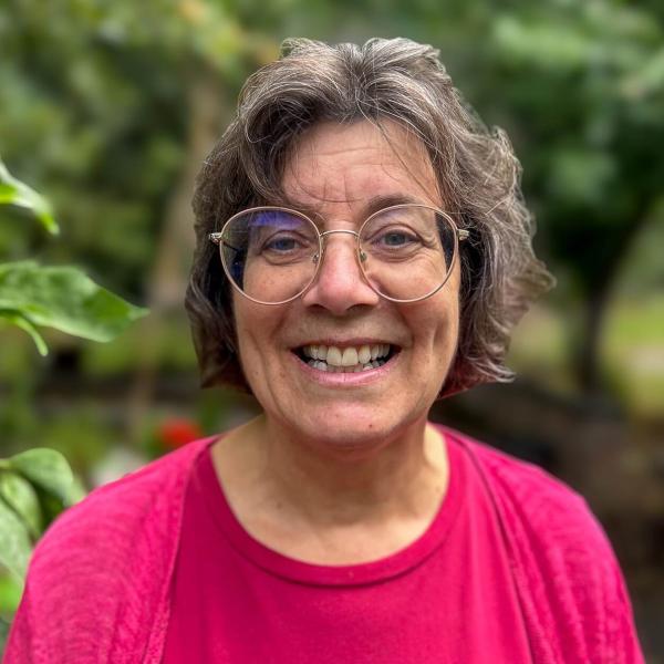 Portrait of Fiona showing a smiley woman wearing a pink shirt against a leafy background.