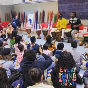 Children sitting on the floor watching an African drumming performance