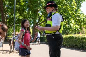 One of Hammersmith & Fulham Council's Law Enforcement Team officers in uniform talking to a little girl in a park.