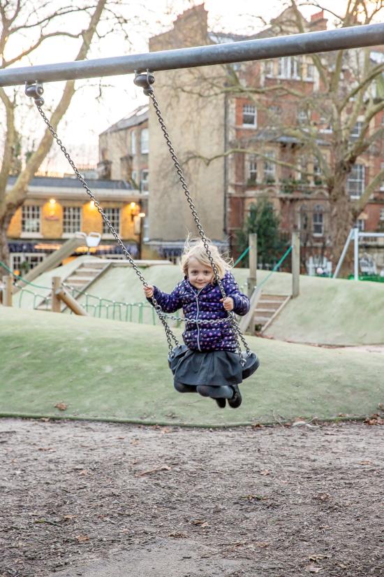 A girl playing on the park's swings in front of the refurbished mounds