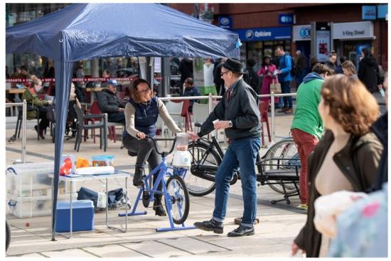 A resident cycles a bicycle juicer at a low-emissions fair.