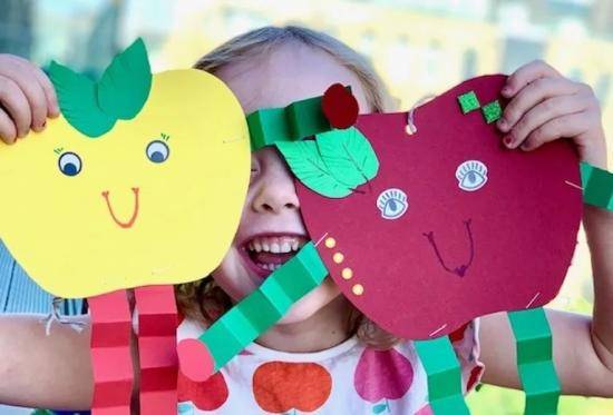 Apple Day crafts - a smiling child holding up colourful paper apple decorations she has cut out and decorated.