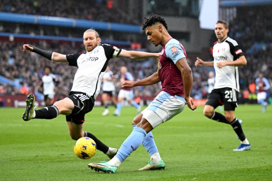 Ollie Watkins of Aston Villa (centre) crosses the ball whilst under pressure from Fulham defender Tim Ream (left)