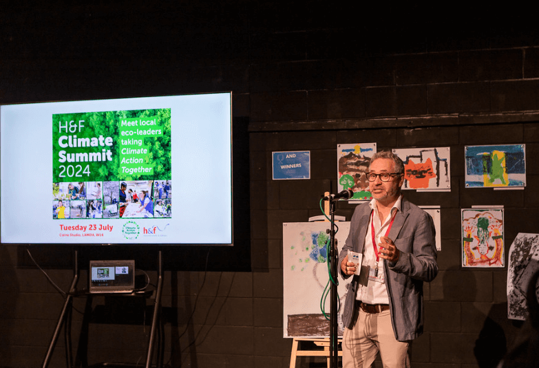 A man standing in front of an audience presenting a talk in front of a screen which says 'H&F Climate Summit 2024'.