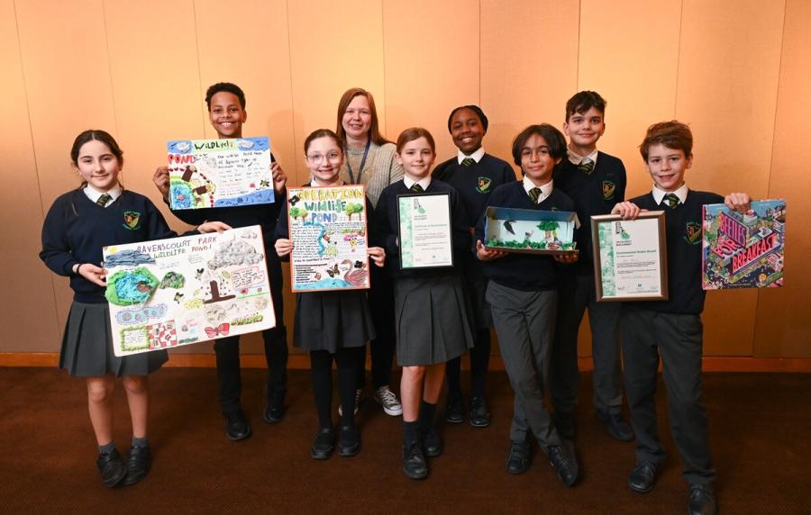 Eight school children with their teacher posing for a photo and holding up their poster designs.