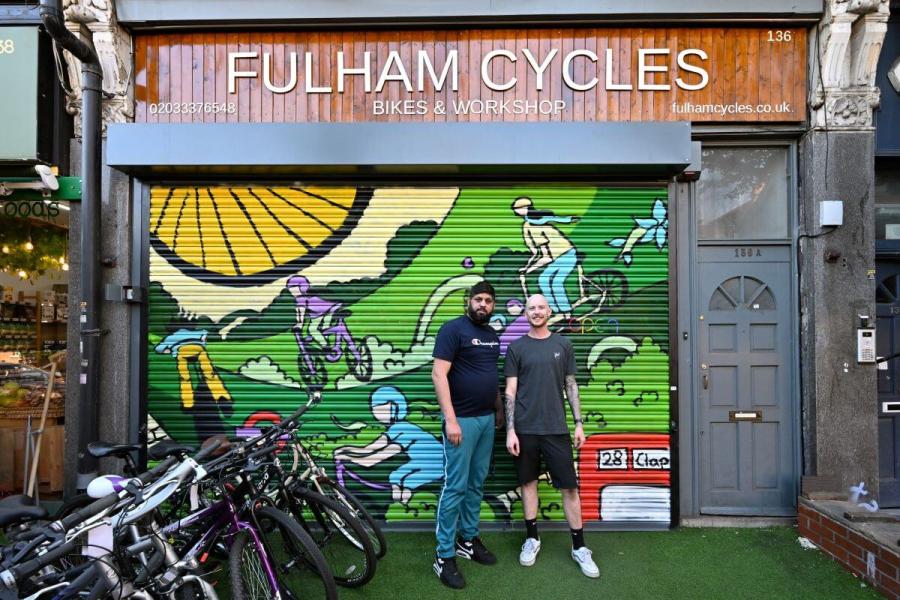 L-R: Atif Habib, owner of Fulham Cycles, stands with a member of staff outside the store's new shutter art