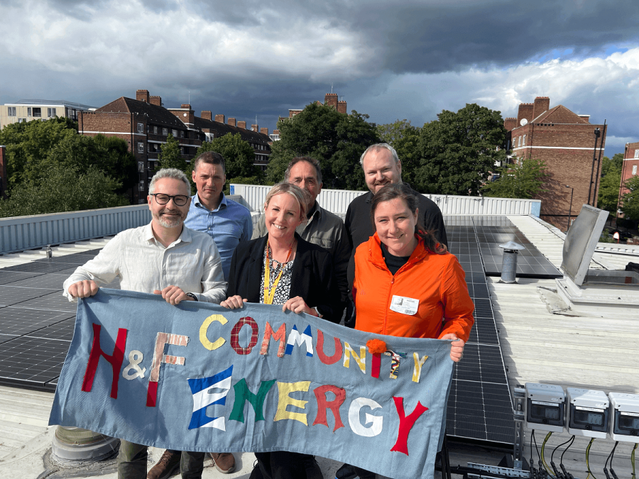 A group of people on a rooftop holding up a sign which says H&F Community Energy.