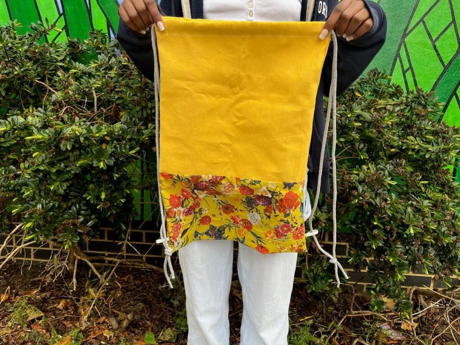 A young person holds a hand-sewn yellow bag.