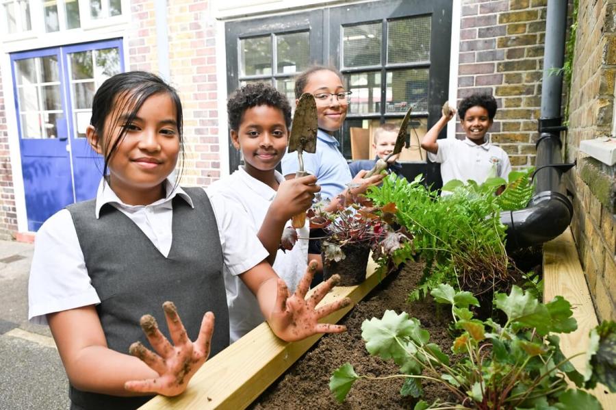 School children smiling at the camera and planting up a wooder planter in their school playground.