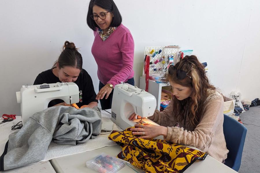 White City resident Marisol from La Modista teaching two young women how to work a sewing machine