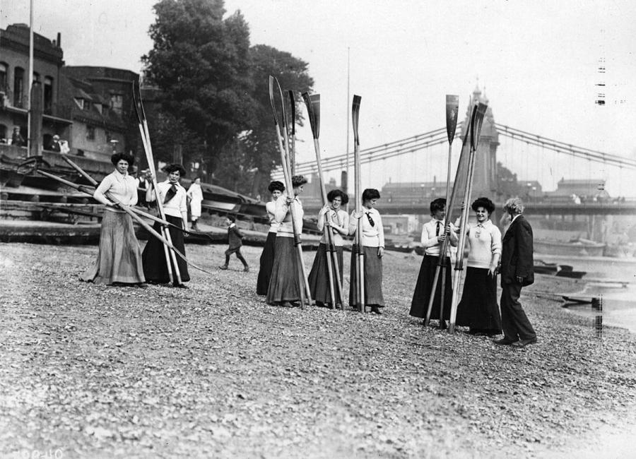 July 1907: All-women crew the Furnivall Rowing Eight on the shore of the Thames - Hammersmith Bridge is in the background