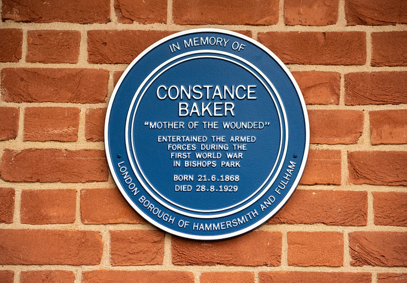 A blue plaque attached to a brick wall - In memory of Constance Baker "Mother of the world"