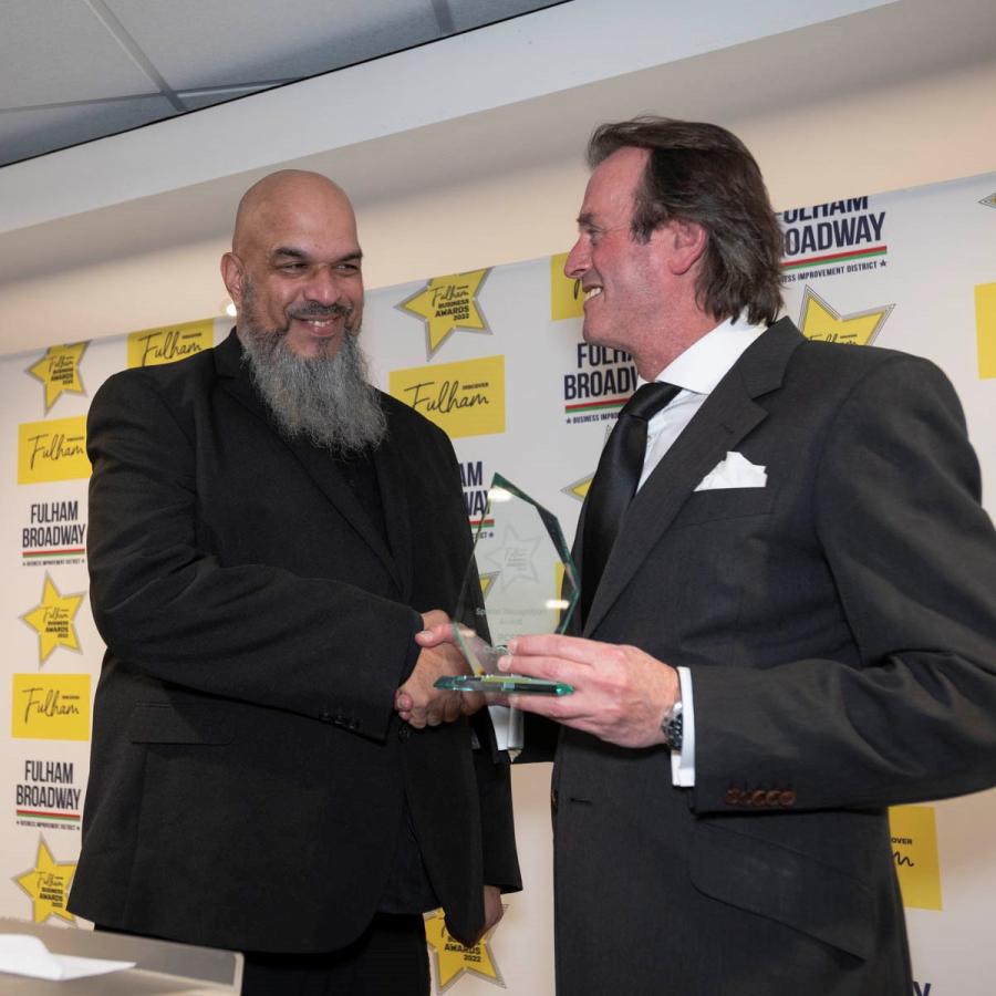 Two men in suits shaking hands, one of them accepting an award