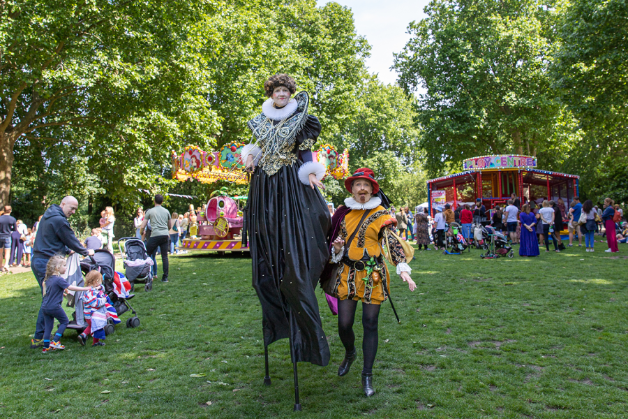 A scene from the Queens Platinum Jubilee celebrations in Bishops Park showing a couple in Elizabethan clothing. The woman is on stilts.